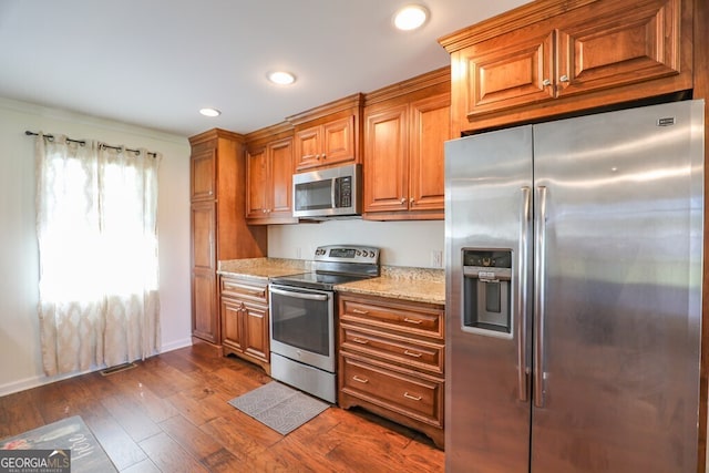 kitchen featuring stainless steel appliances, light stone countertops, and dark hardwood / wood-style floors