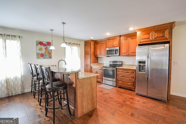 kitchen featuring dark wood-type flooring, a breakfast bar area, hanging light fixtures, stainless steel appliances, and light stone countertops