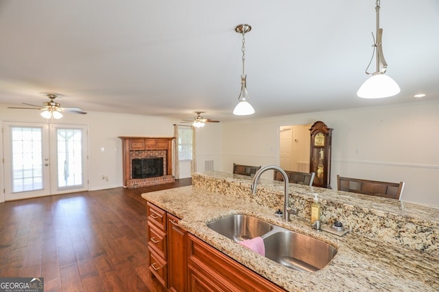 kitchen with pendant lighting, a fireplace, sink, dark hardwood / wood-style flooring, and light stone counters