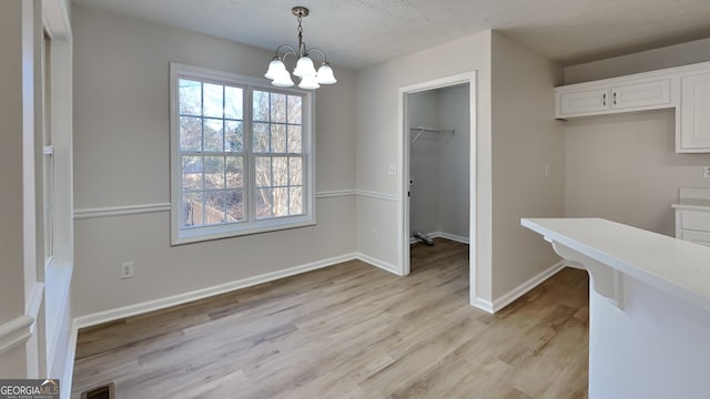 unfurnished dining area featuring a notable chandelier, light hardwood / wood-style flooring, and a textured ceiling