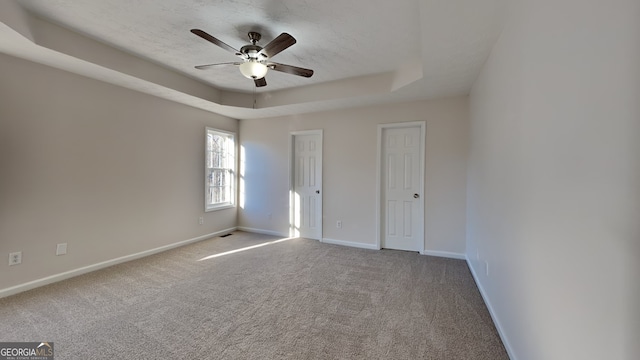 spare room with a tray ceiling, ceiling fan, and carpet