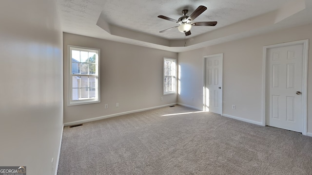 spare room with a tray ceiling, plenty of natural light, light colored carpet, and ceiling fan