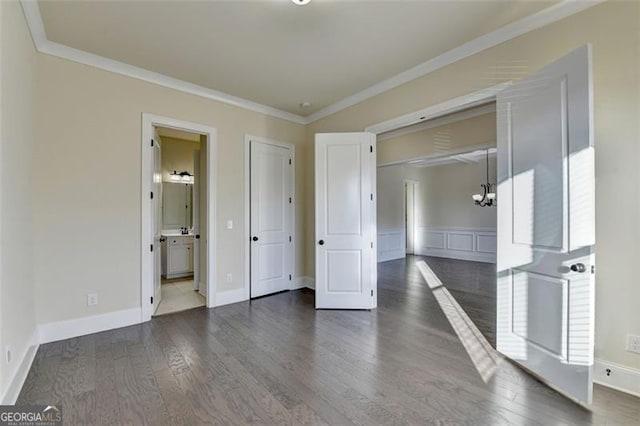 unfurnished bedroom with an inviting chandelier, crown molding, dark wood-type flooring, and ensuite bathroom