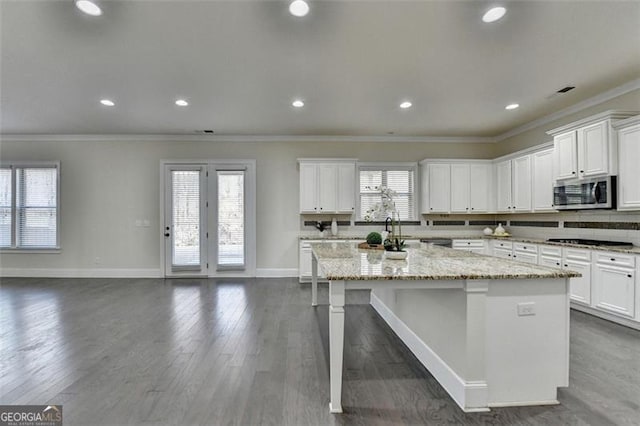 kitchen featuring a wealth of natural light, white cabinetry, ornamental molding, a kitchen island with sink, and light stone counters