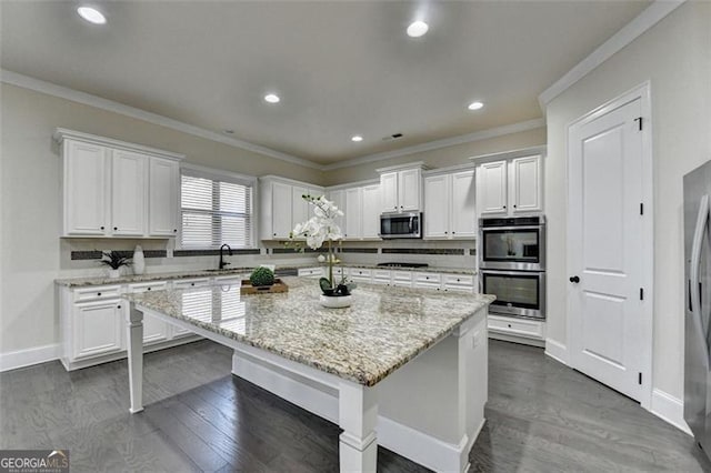 kitchen featuring white cabinetry, crown molding, appliances with stainless steel finishes, a kitchen island, and light stone countertops