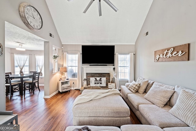 living room featuring wood-type flooring, a stone fireplace, a textured ceiling, and a wealth of natural light