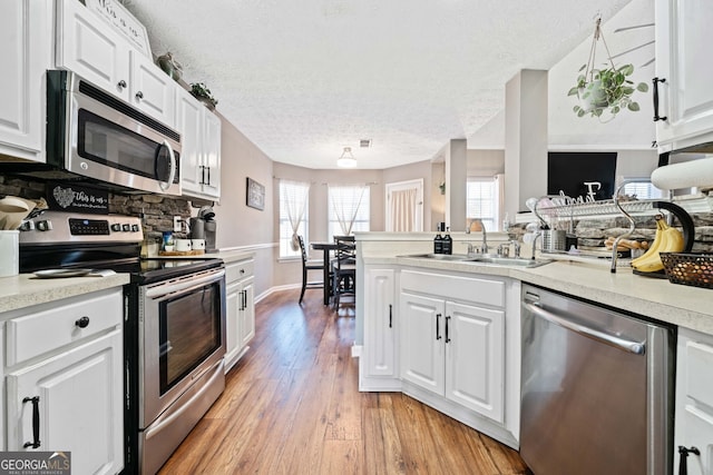 kitchen with sink, stainless steel appliances, a textured ceiling, white cabinets, and light wood-type flooring