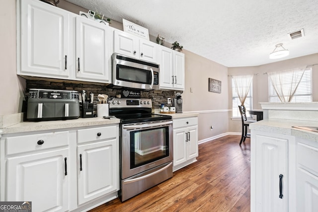 kitchen featuring white cabinetry, stainless steel appliances, wood-type flooring, and backsplash