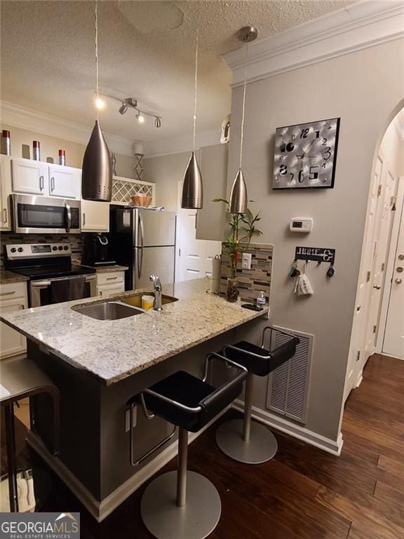 kitchen featuring stainless steel appliances, hanging light fixtures, white cabinets, and a kitchen breakfast bar