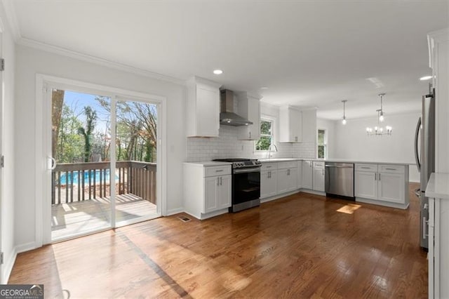 kitchen with appliances with stainless steel finishes, white cabinets, dark hardwood / wood-style flooring, hanging light fixtures, and wall chimney range hood