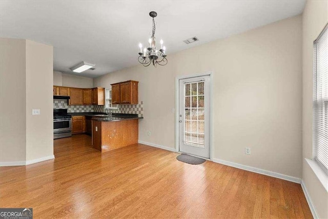 kitchen with stainless steel stove, sink, backsplash, a chandelier, and light hardwood / wood-style flooring