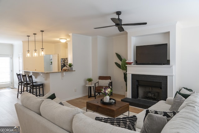 living room with a fireplace, light hardwood / wood-style flooring, ornamental molding, and ceiling fan