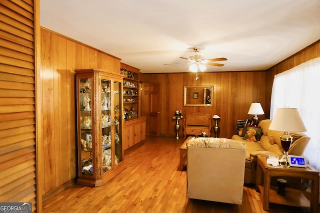 living room featuring ceiling fan, wooden walls, and light hardwood / wood-style flooring