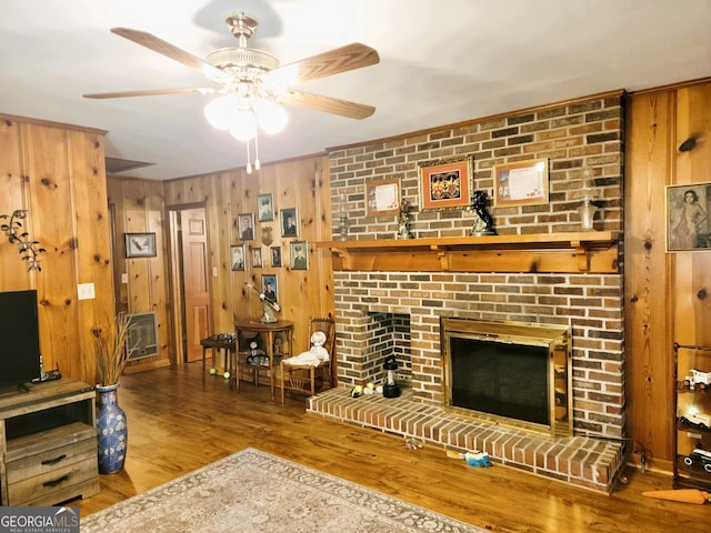 living room with a brick fireplace, hardwood / wood-style flooring, ceiling fan, and wood walls