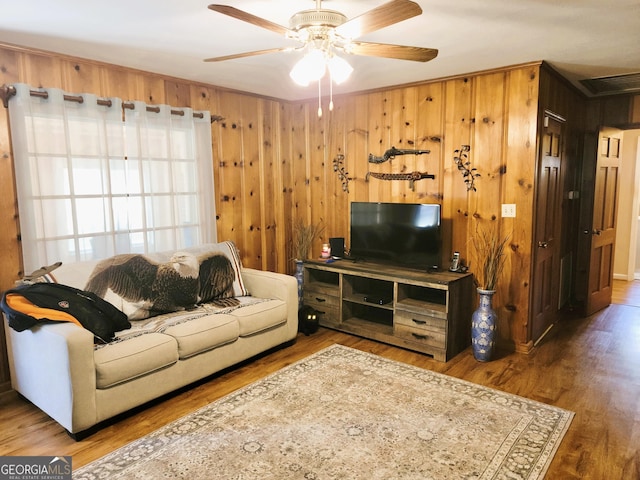 living room with wood-type flooring, wooden walls, crown molding, and ceiling fan