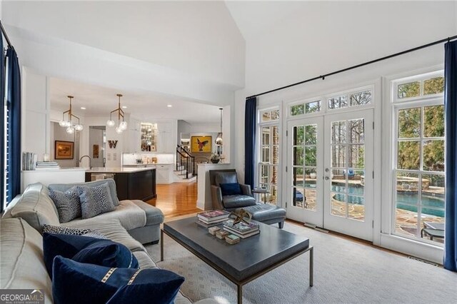 living room featuring french doors, a towering ceiling, a chandelier, and light hardwood / wood-style flooring