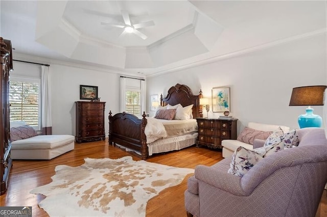 bedroom featuring multiple windows, hardwood / wood-style flooring, crown molding, and a raised ceiling