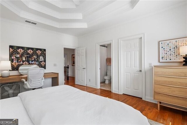 bedroom with hardwood / wood-style flooring, ensuite bath, ornamental molding, and a raised ceiling