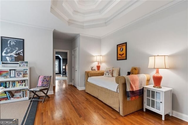 bedroom featuring a raised ceiling, ornamental molding, and wood-type flooring