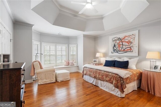 bedroom featuring a fireplace, wood-type flooring, ornamental molding, ceiling fan, and a tray ceiling