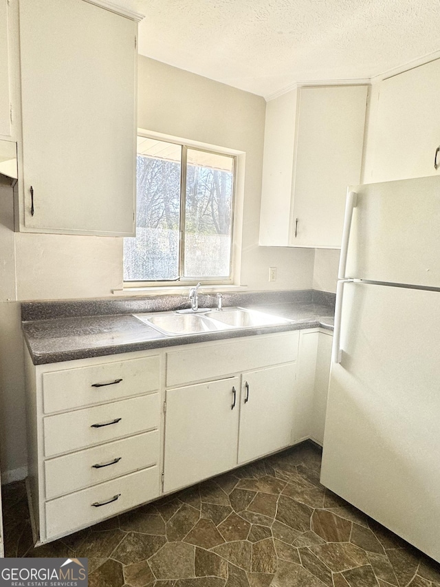 kitchen with white fridge, sink, white cabinets, and a textured ceiling