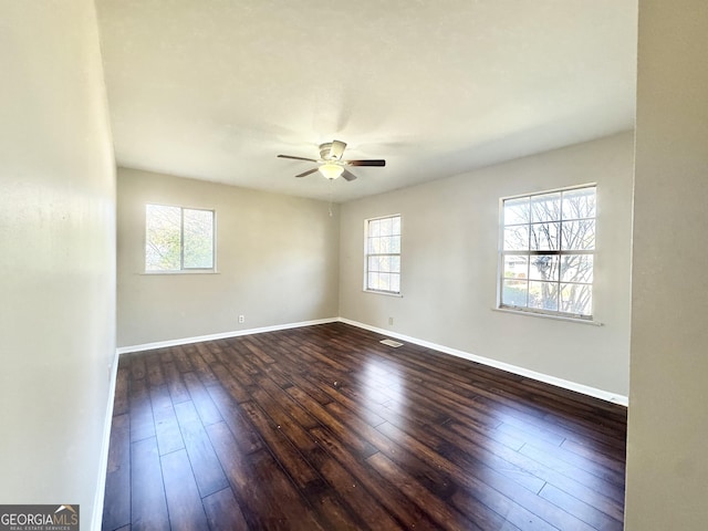 empty room with dark wood-type flooring, ceiling fan, and a wealth of natural light