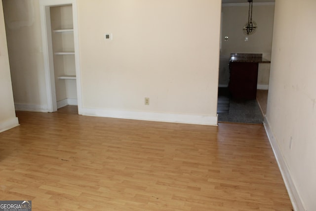 spare room with built in shelves and light hardwood / wood-style flooring