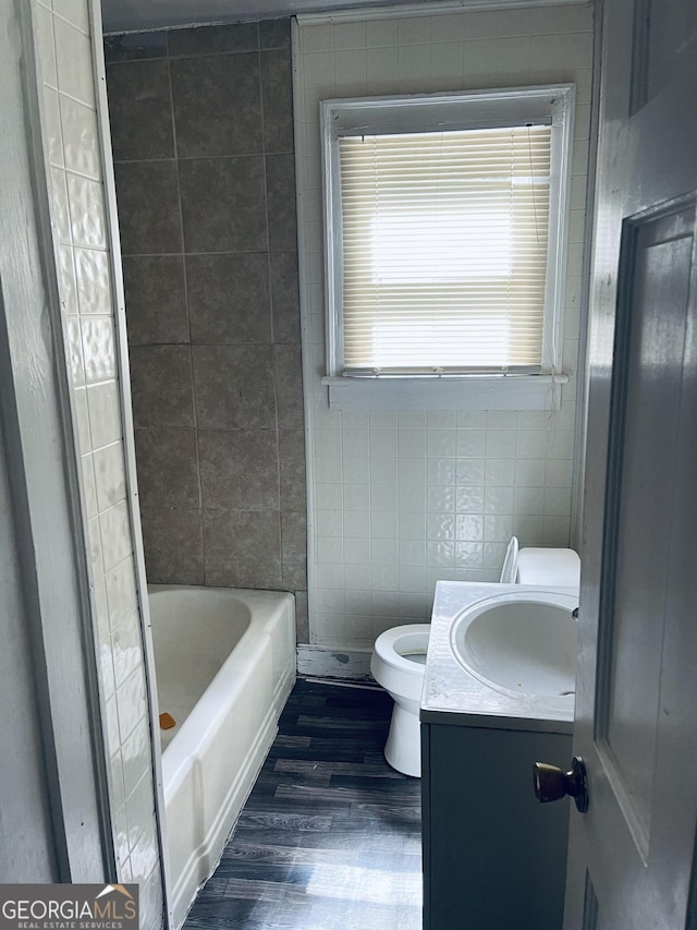 bathroom with tile walls, a tub to relax in, hardwood / wood-style flooring, vanity, and toilet