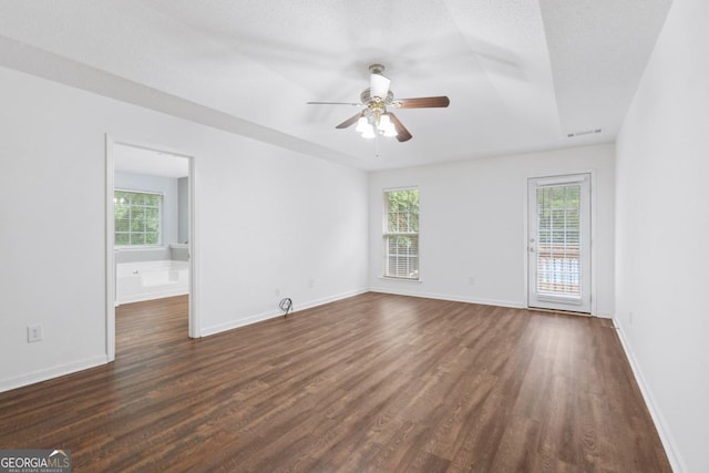 spare room featuring ceiling fan, a textured ceiling, dark wood-type flooring, and a healthy amount of sunlight