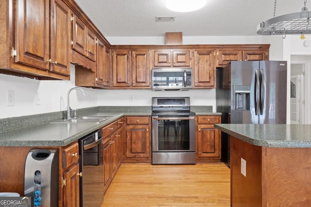 kitchen featuring appliances with stainless steel finishes, sink, a textured ceiling, and light wood-type flooring