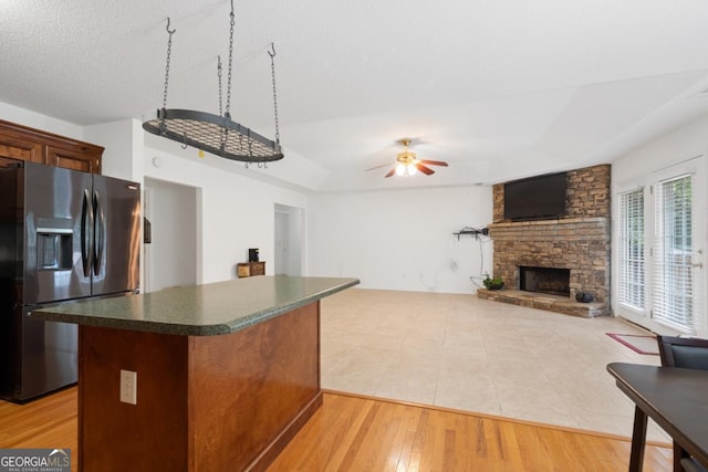 kitchen with stainless steel refrigerator with ice dispenser, a center island, light wood-type flooring, ceiling fan, and a fireplace