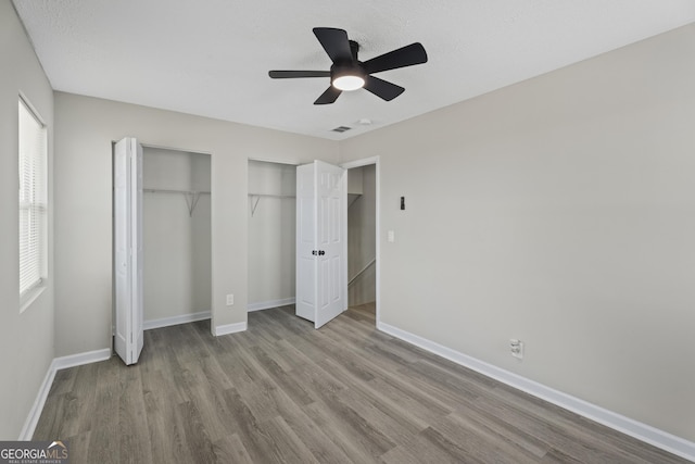 unfurnished bedroom with visible vents, ceiling fan, baseboards, multiple closets, and wood finished floors