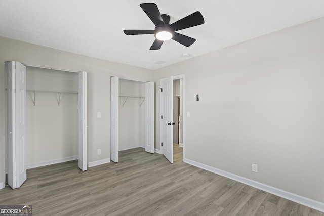 unfurnished bedroom featuring baseboards, two closets, light wood-style flooring, and a ceiling fan