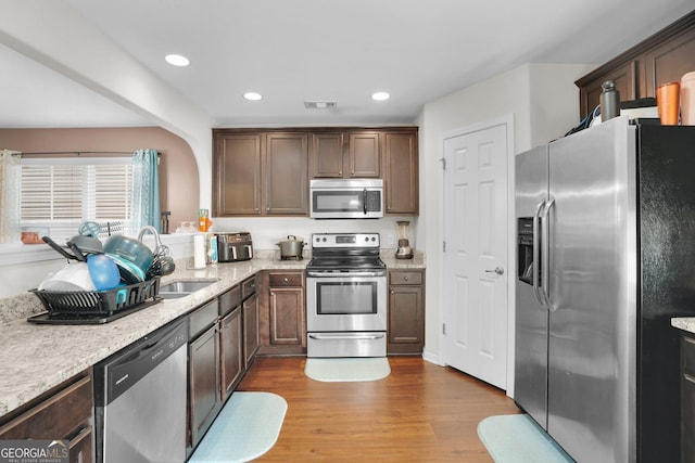 kitchen with dark brown cabinetry, stainless steel appliances, sink, and light hardwood / wood-style flooring