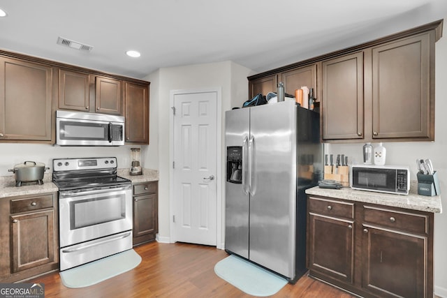 kitchen with hardwood / wood-style flooring, appliances with stainless steel finishes, light stone counters, and dark brown cabinets