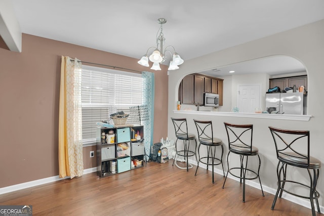 kitchen featuring light hardwood / wood-style flooring, appliances with stainless steel finishes, hanging light fixtures, dark brown cabinets, and a notable chandelier