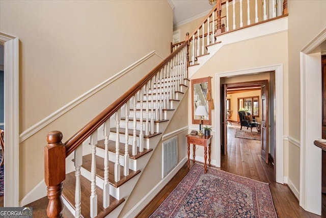 staircase with a high ceiling, wood-type flooring, and ornamental molding