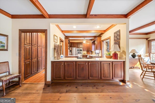 kitchen featuring beamed ceiling, stainless steel appliances, kitchen peninsula, and light hardwood / wood-style floors