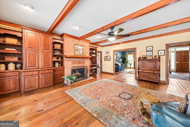 living room featuring ceiling fan, beam ceiling, a brick fireplace, and light wood-type flooring