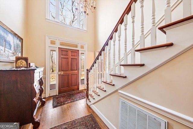 entryway with hardwood / wood-style floors, a towering ceiling, and a chandelier