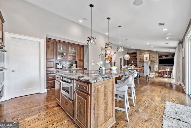 kitchen featuring hardwood / wood-style flooring, dark stone countertops, hanging light fixtures, a kitchen breakfast bar, and an island with sink