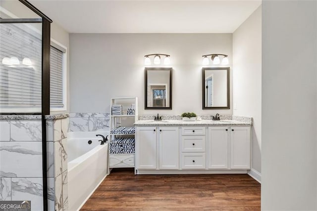 full bath with wood finished floors, double vanity, a sink, and a bath