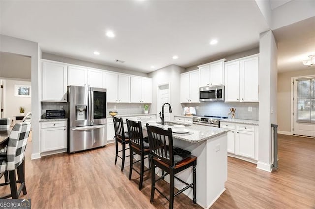 kitchen with stainless steel appliances, a sink, white cabinets, light wood-type flooring, and a kitchen bar