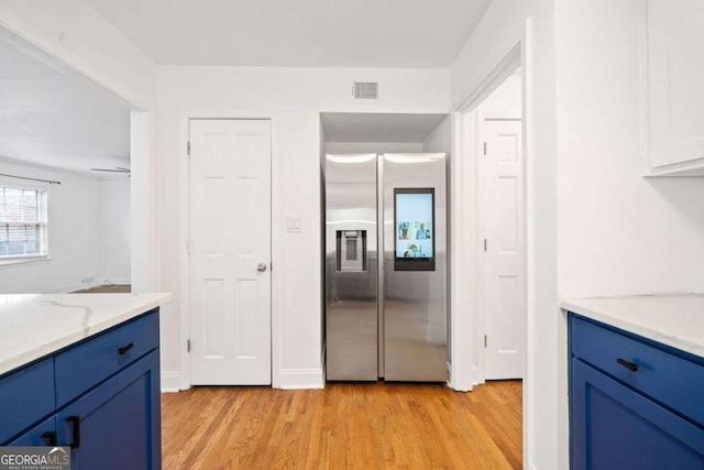 kitchen with light stone counters, stainless steel fridge, light hardwood / wood-style floors, and blue cabinetry