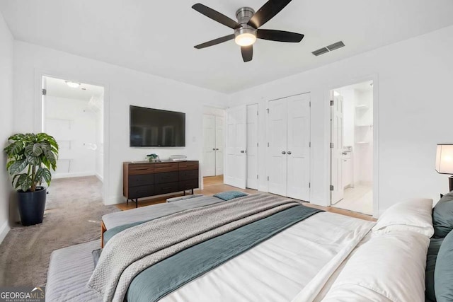 carpeted bedroom with multiple closets, ceiling fan, and ensuite bath