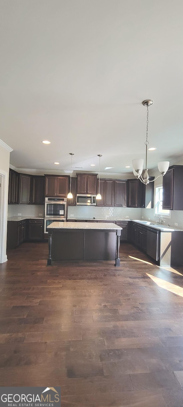 kitchen with appliances with stainless steel finishes, sink, dark hardwood / wood-style floors, hanging light fixtures, and dark brown cabinetry