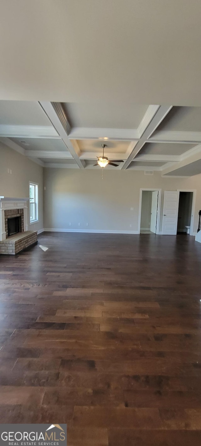 unfurnished living room featuring beam ceiling, ceiling fan, coffered ceiling, a fireplace, and dark hardwood / wood-style flooring