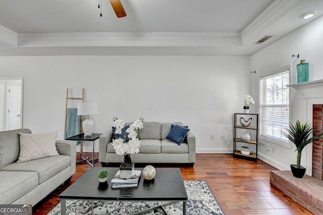 living room with dark hardwood / wood-style flooring, a tray ceiling, ornamental molding, and ceiling fan