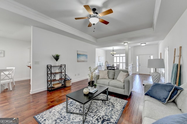 living room with dark hardwood / wood-style flooring, a tray ceiling, ceiling fan with notable chandelier, and ornamental molding