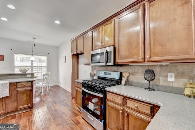 kitchen with pendant lighting, appliances with stainless steel finishes, hardwood / wood-style floors, and decorative backsplash